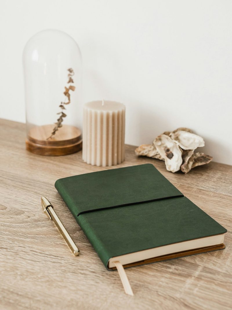 A green notebook and pen on a wooden table