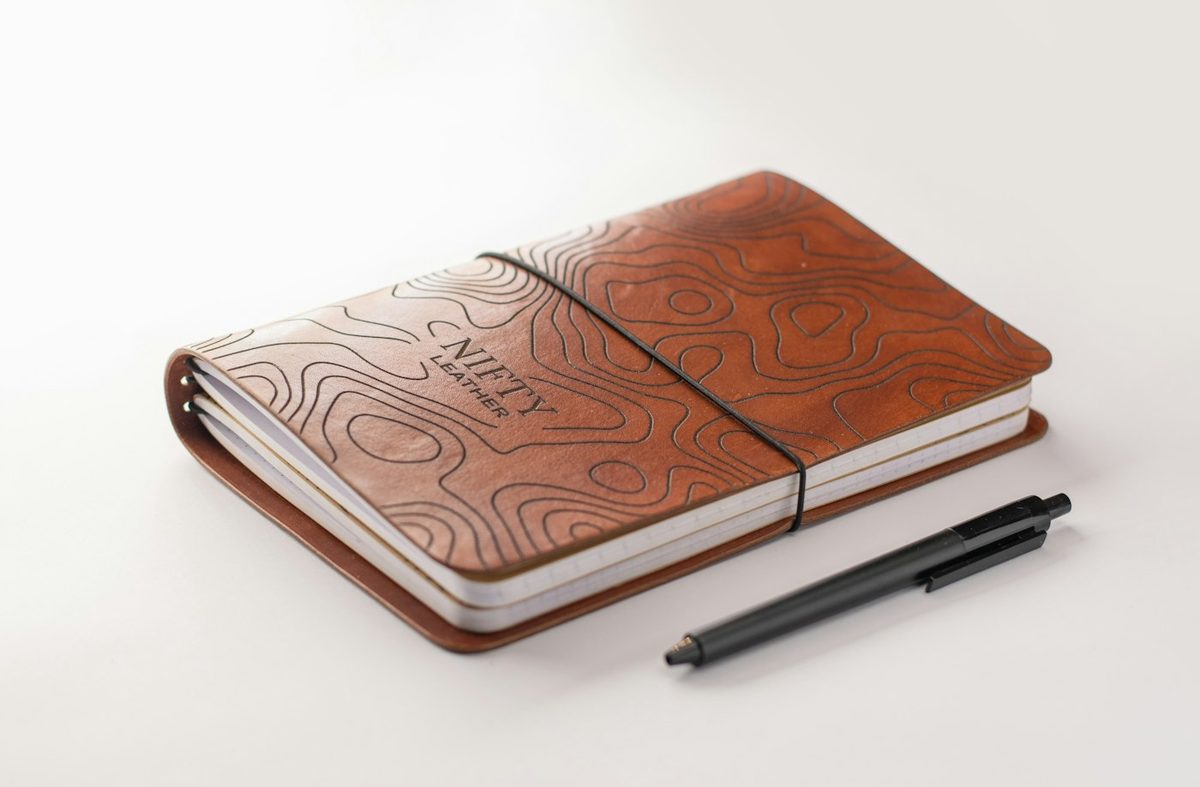 A tan leather notebook with an embossed cover and a pen